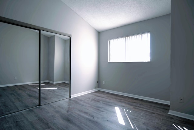 unfurnished bedroom with dark wood-type flooring, a textured ceiling, a closet, and vaulted ceiling