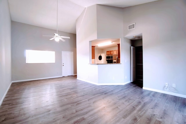 unfurnished living room with ceiling fan, wood-type flooring, and a towering ceiling