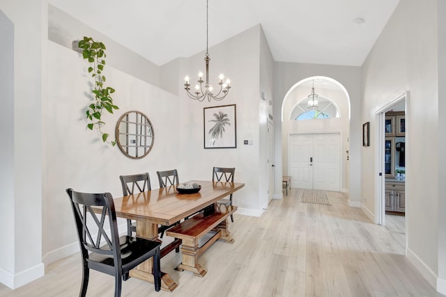 dining space featuring a towering ceiling, a notable chandelier, and light wood-type flooring