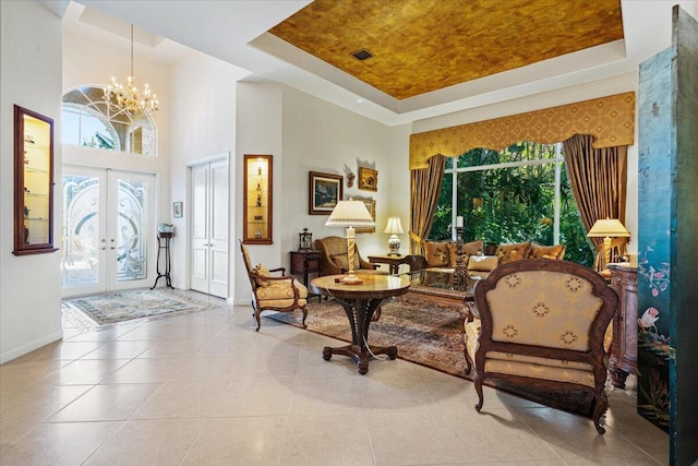 tiled entryway featuring a raised ceiling, a towering ceiling, a chandelier, and french doors