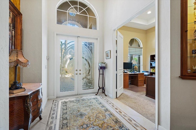 foyer entrance with light tile patterned floors, a towering ceiling, and french doors