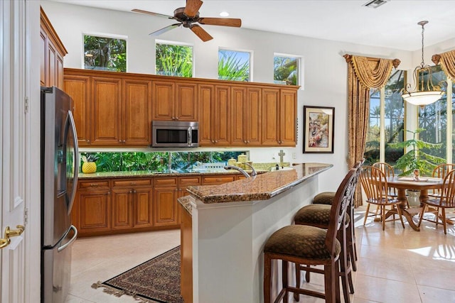 kitchen with a breakfast bar, appliances with stainless steel finishes, pendant lighting, light stone countertops, and backsplash