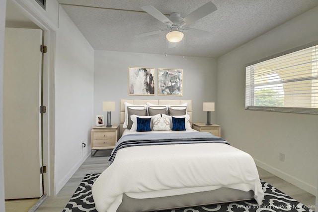 bedroom with ceiling fan, light hardwood / wood-style floors, and a textured ceiling