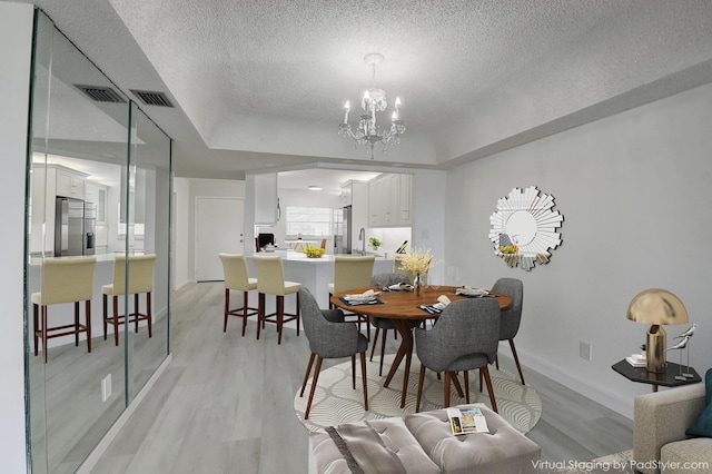 dining room featuring a textured ceiling, light wood-type flooring, sink, an inviting chandelier, and a tray ceiling