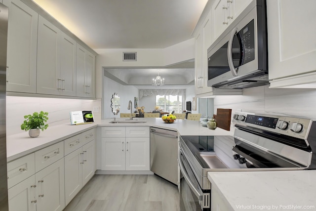 kitchen with appliances with stainless steel finishes, hanging light fixtures, sink, white cabinets, and backsplash