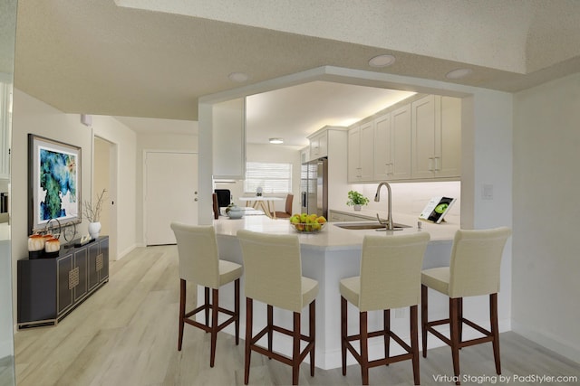 kitchen with white cabinetry, sink, light wood-type flooring, kitchen peninsula, and stainless steel fridge