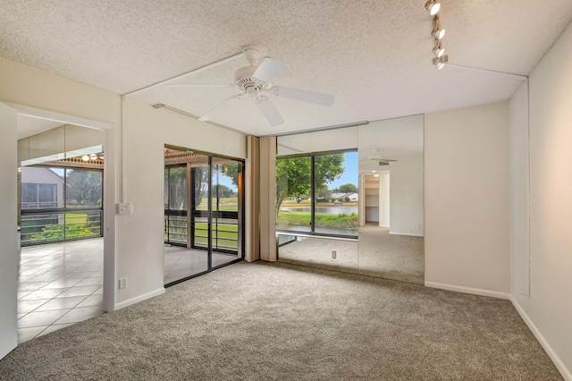 carpeted empty room featuring a textured ceiling, a wealth of natural light, track lighting, and ceiling fan