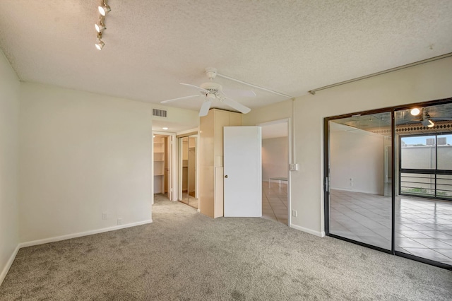 unfurnished bedroom with a spacious closet, light colored carpet, ceiling fan, a textured ceiling, and a closet