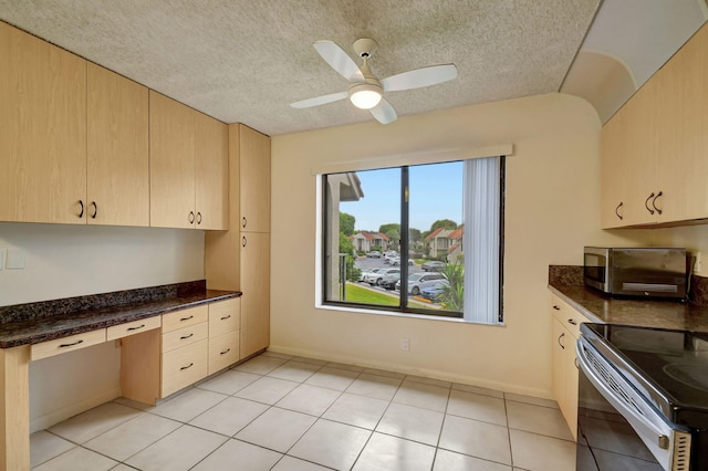 kitchen featuring built in desk, light brown cabinetry, dark stone countertops, ceiling fan, and stainless steel appliances