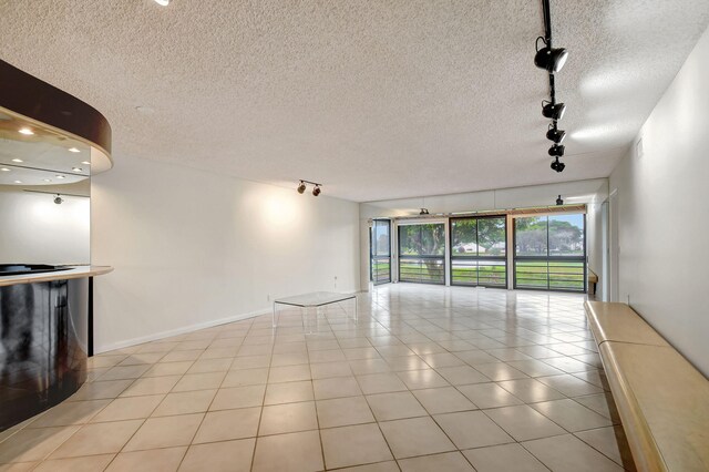 5519 Fairway Park Dr Unit 202, Boynton Beach, FL 33437 - unfurnished living room with rail lighting, a textured ceiling, light tile patterned floors, and baseboards