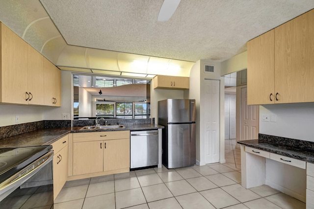 kitchen with light brown cabinetry, sink, dark stone countertops, light tile patterned floors, and stainless steel appliances