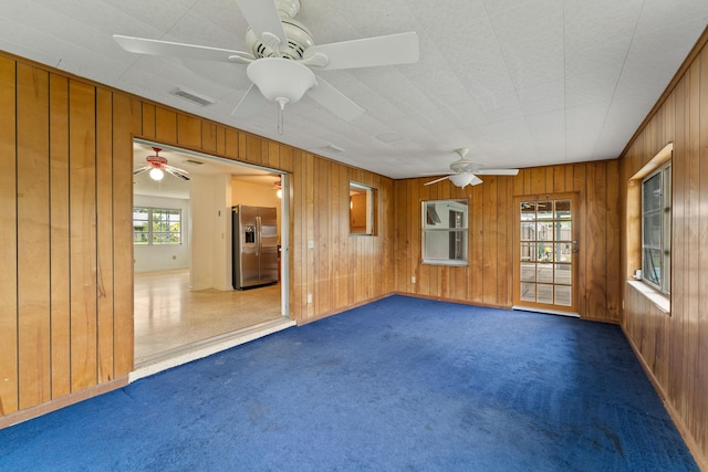 carpeted empty room with ceiling fan and wooden walls