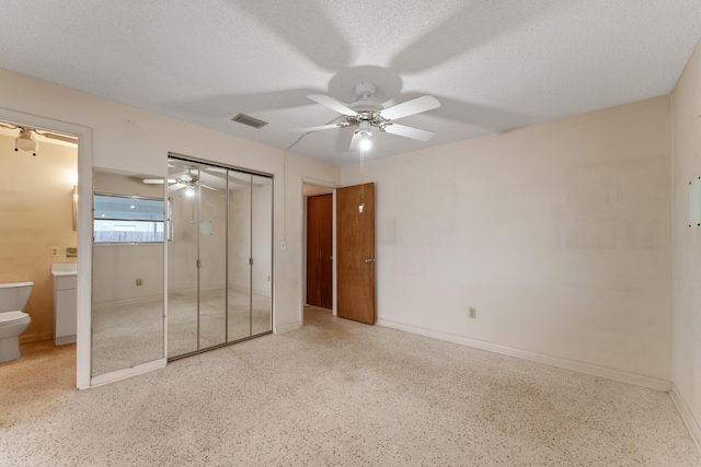 unfurnished bedroom with ceiling fan, a textured ceiling, ensuite bathroom, and a closet