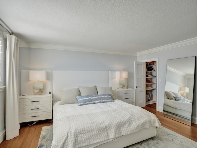 bedroom featuring wood-type flooring, a walk in closet, a textured ceiling, and crown molding