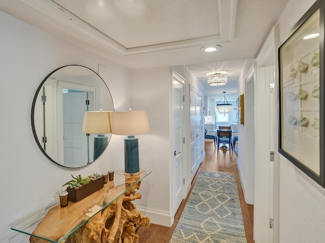 hall with a chandelier, a tray ceiling, wood finished floors, and baseboards