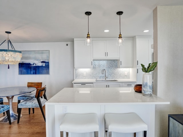 kitchen featuring sink, white cabinetry, light stone counters, decorative backsplash, and decorative light fixtures