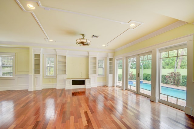 unfurnished living room featuring built in shelves, crown molding, hardwood / wood-style floors, and french doors