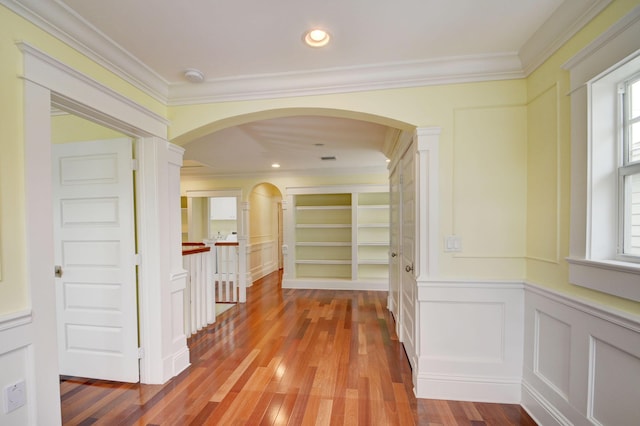 corridor featuring built in features, a wealth of natural light, ornamental molding, and wood-type flooring