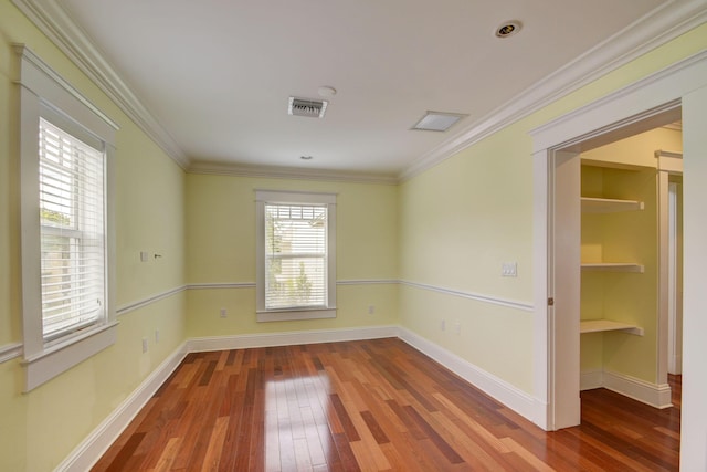 empty room featuring wood-type flooring, built in features, and crown molding