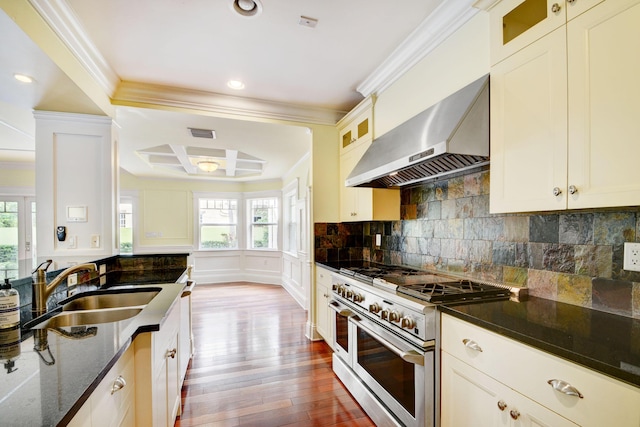 kitchen featuring sink, dark stone counters, range with two ovens, wall chimney range hood, and coffered ceiling