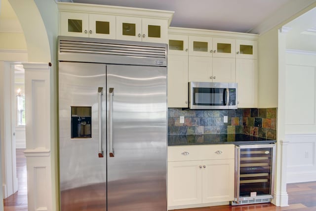 kitchen with beverage cooler, stainless steel appliances, decorative backsplash, hardwood / wood-style flooring, and crown molding