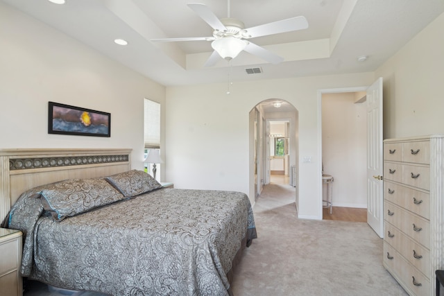 bedroom featuring ceiling fan, a tray ceiling, light colored carpet, and multiple windows