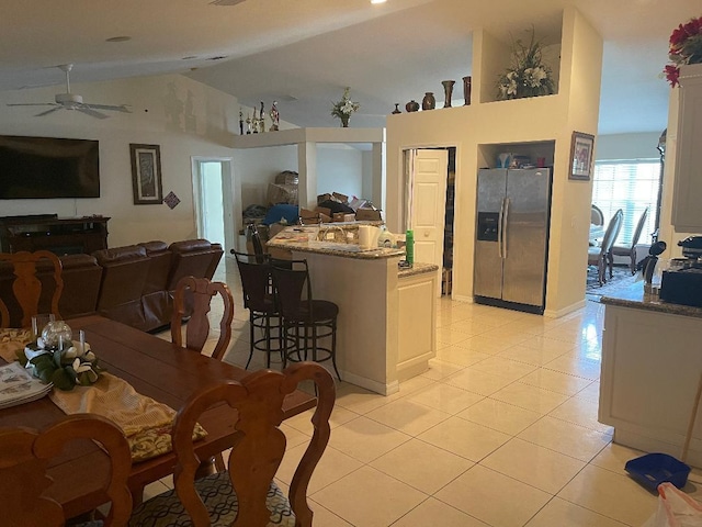 kitchen with a kitchen breakfast bar, stainless steel fridge, white cabinetry, light tile patterned floors, and stone counters