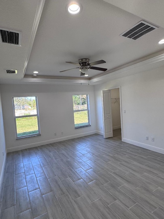 spare room featuring a raised ceiling, crown molding, and light wood-type flooring