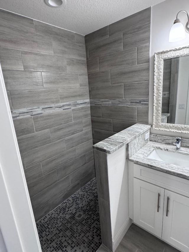 bathroom with vanity, a textured ceiling, and tiled shower