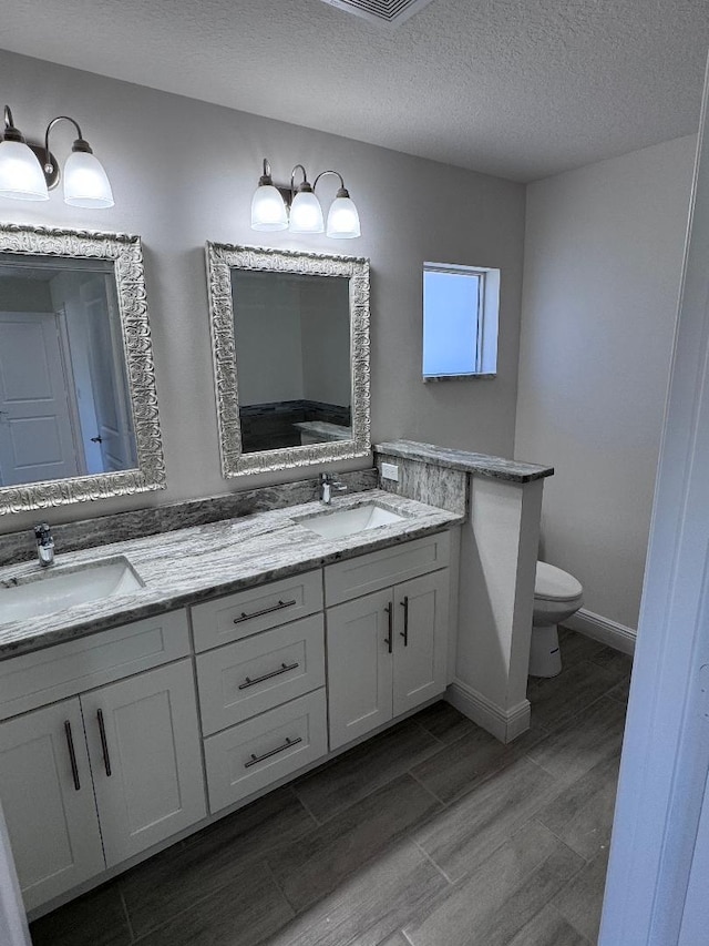 bathroom with hardwood / wood-style flooring, vanity, a textured ceiling, and toilet