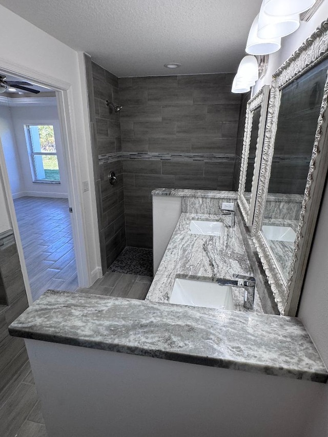 bathroom with a textured ceiling, a tile shower, vanity, hardwood / wood-style flooring, and ceiling fan