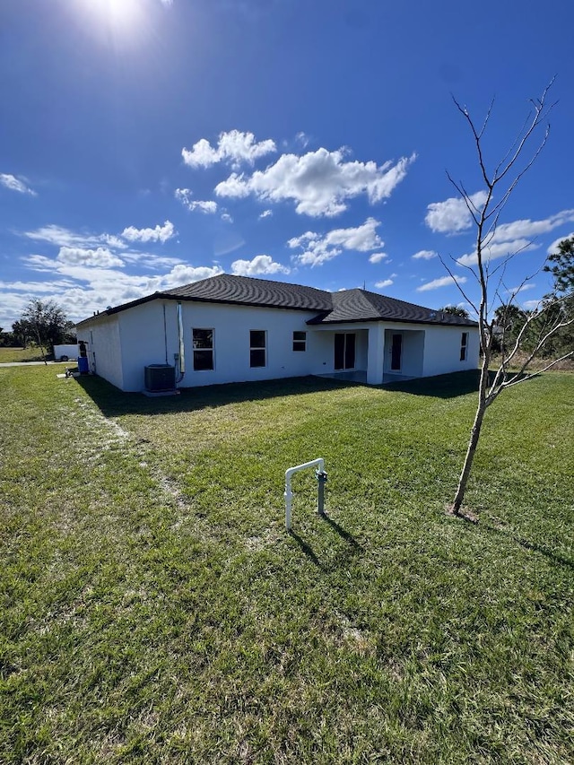 rear view of house featuring central AC and a lawn