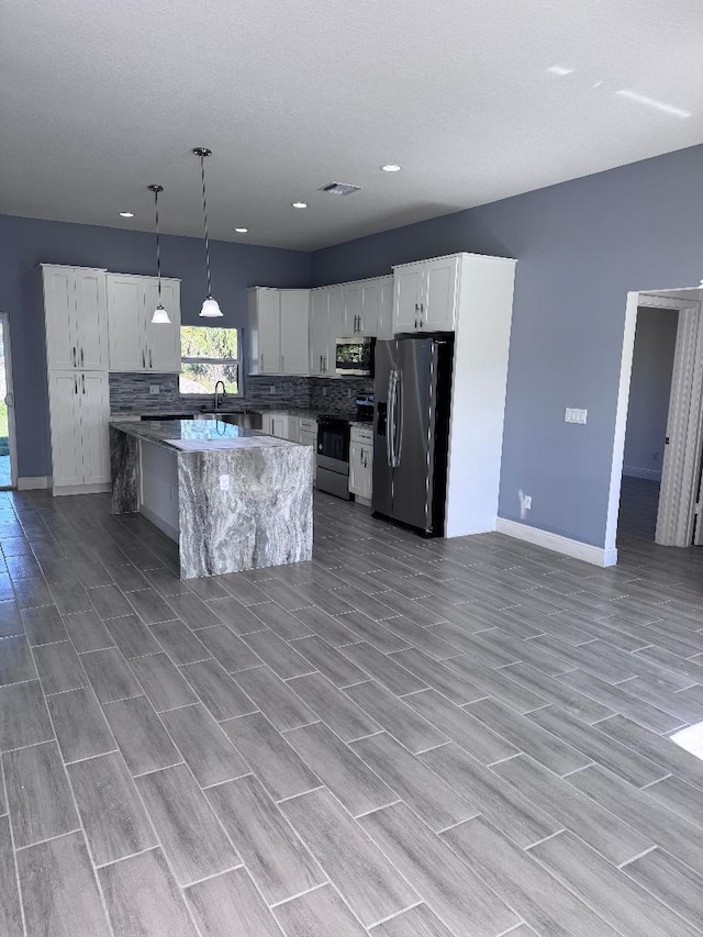 kitchen featuring appliances with stainless steel finishes, decorative backsplash, white cabinets, a kitchen island, and decorative light fixtures