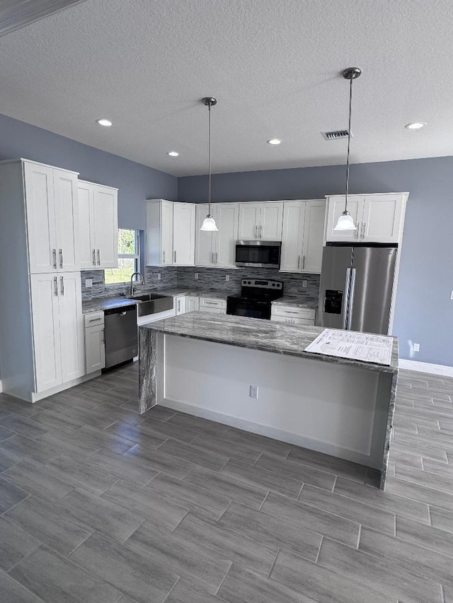 kitchen with white cabinetry, stainless steel appliances, decorative light fixtures, and a kitchen island