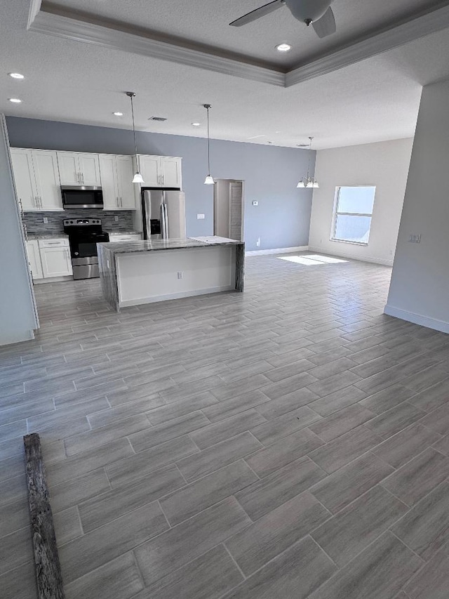 kitchen with appliances with stainless steel finishes, white cabinetry, an island with sink, hanging light fixtures, and a tray ceiling