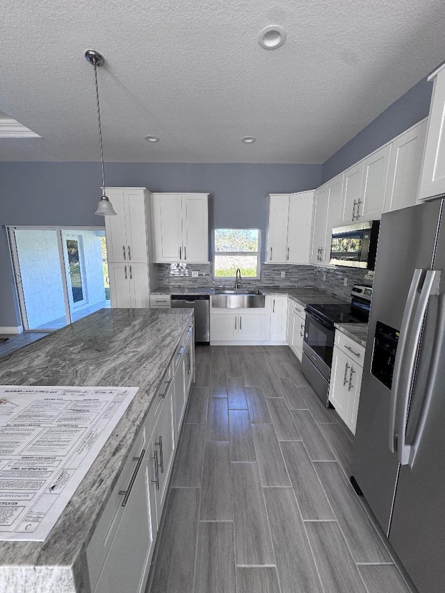 kitchen with sink, white cabinetry, decorative light fixtures, stainless steel appliances, and backsplash