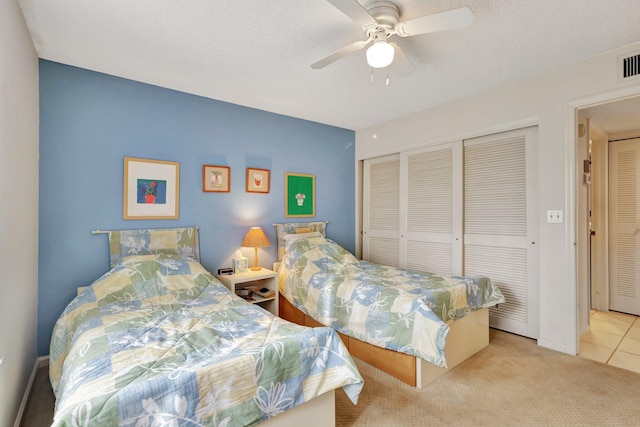 bedroom with ceiling fan, light colored carpet, a closet, and a textured ceiling