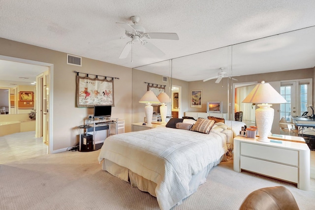 bedroom featuring ceiling fan, light carpet, a textured ceiling, and ensuite bath