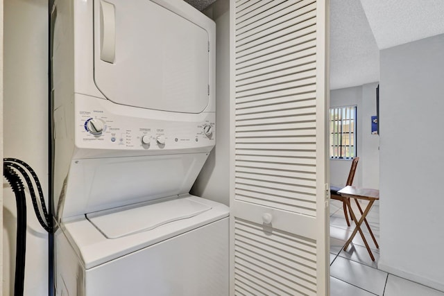 laundry area featuring stacked washer / drying machine, a textured ceiling, and light tile patterned floors