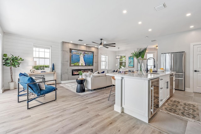 kitchen with an island with sink, sink, white cabinets, beverage cooler, and a tiled fireplace