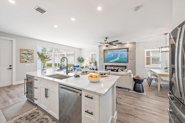 kitchen with sink, white cabinetry, appliances with stainless steel finishes, beverage cooler, and light stone countertops