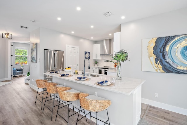 kitchen with white cabinetry, sink, wall chimney range hood, stainless steel appliances, and a center island with sink