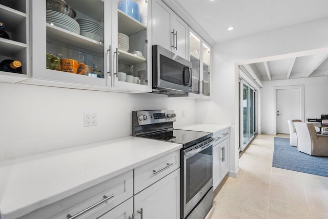 kitchen with beam ceiling, light tile patterned floors, stainless steel appliances, light countertops, and white cabinets