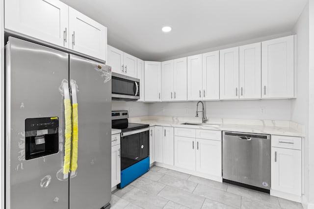 kitchen with stainless steel appliances, white cabinetry, sink, and light stone counters