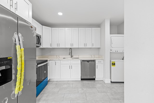 kitchen featuring appliances with stainless steel finishes, stacked washer / dryer, sink, and white cabinets