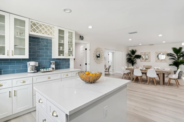 kitchen with light stone countertops, a kitchen island, white cabinetry, tasteful backsplash, and light hardwood / wood-style flooring