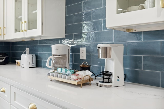 interior details with backsplash, white cabinets, and light stone countertops