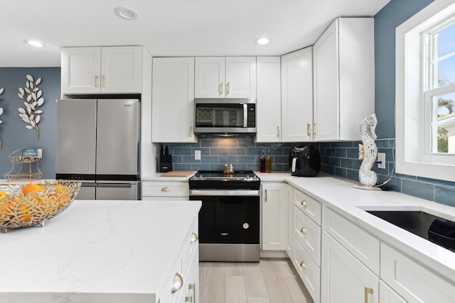 kitchen with appliances with stainless steel finishes, white cabinetry, tasteful backsplash, light stone counters, and light hardwood / wood-style flooring