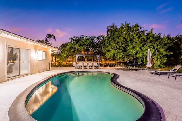 pool at dusk featuring a patio area and a gazebo