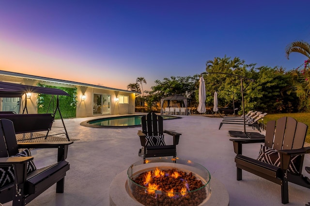 pool at dusk featuring a fire pit, a gazebo, and a patio